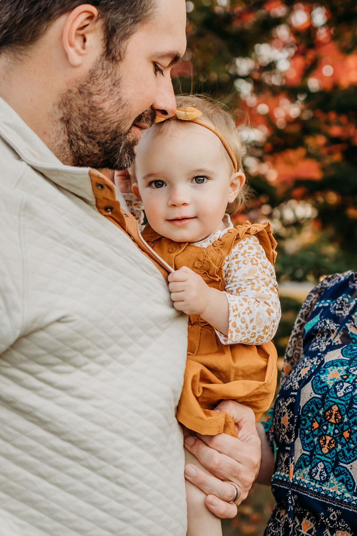 An Eau Claire family photo session of  a baby girl holding dad's shirt and looking at camera near
