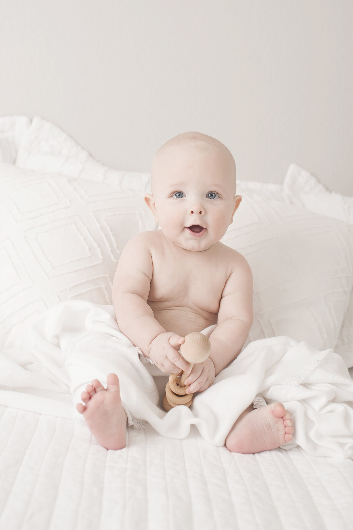 six month old baby sitting on white baby with wooden toy