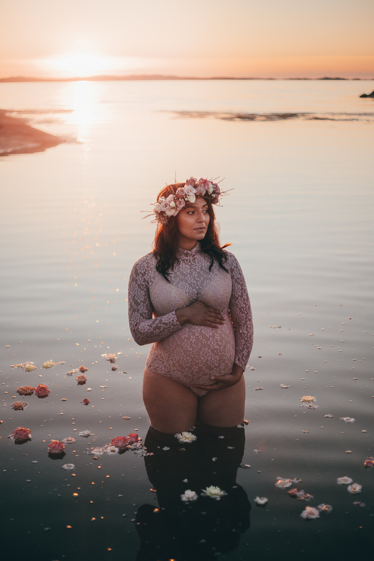 en gravid mamma sitter i vattnet i en rosa body med blommor i hennes hår