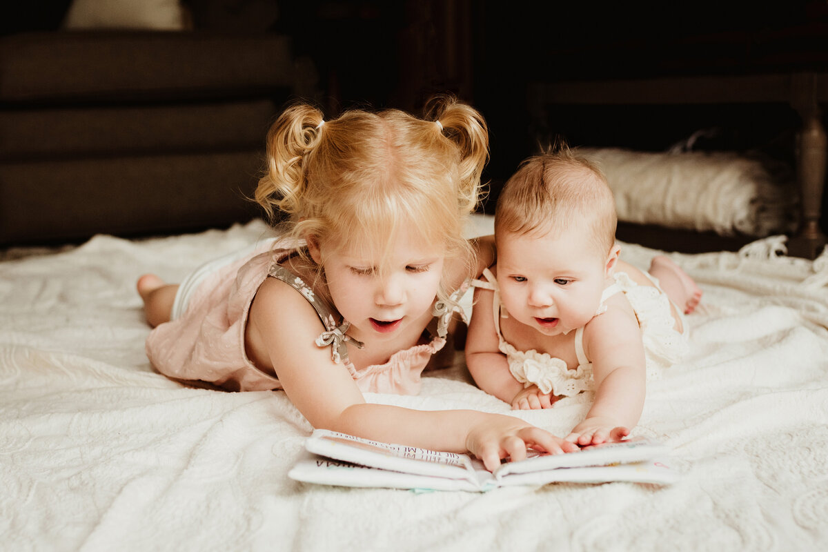 Sisters lying on the floor together look through a book.
