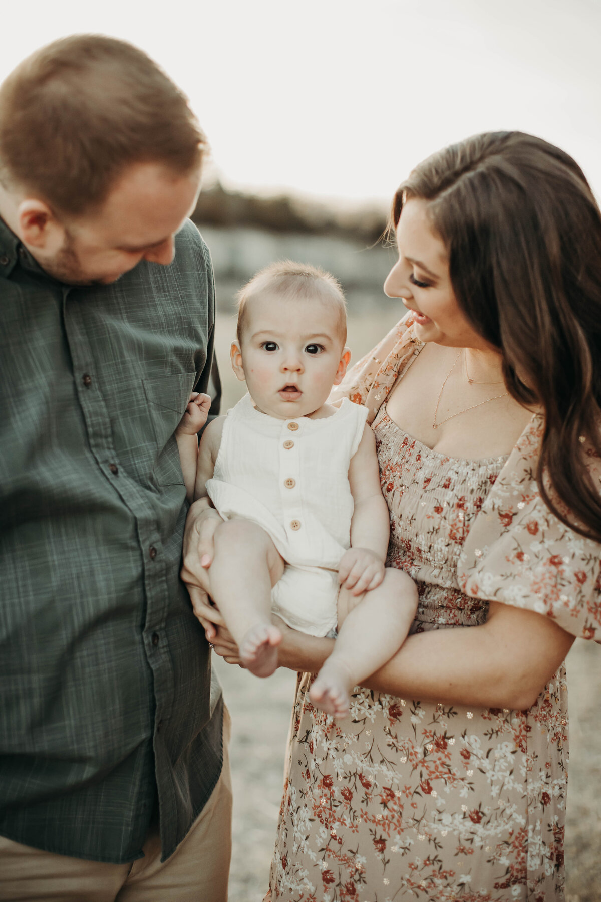 Golden hour portrait of parents cradling their baby boy, all bathed in warm light.