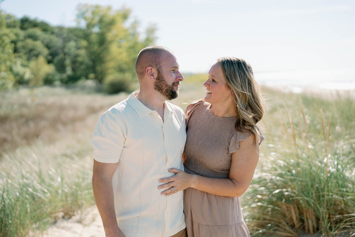 A mom and dad smiling at each other in the dune grass at Weko Beach during their Bridgman Michigan family mini session.