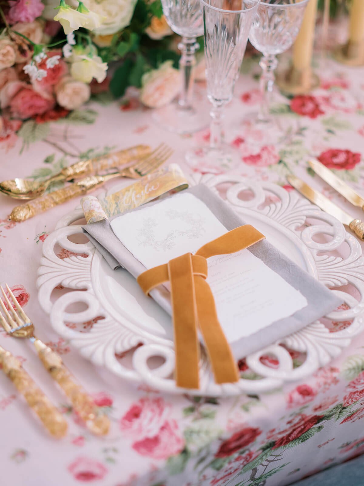 wedding dinner place setting with pink floral patterned linen and napkin tied with an ochre velvet bow on a white charger plate at blenheim palace