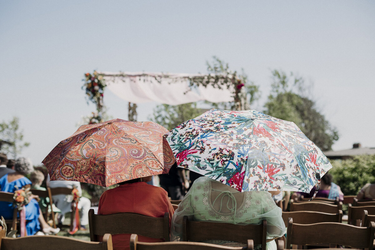 Two women sitting under colorful umbrellas at an Indian wedding ceremony. Photo by Mira Park Photography.