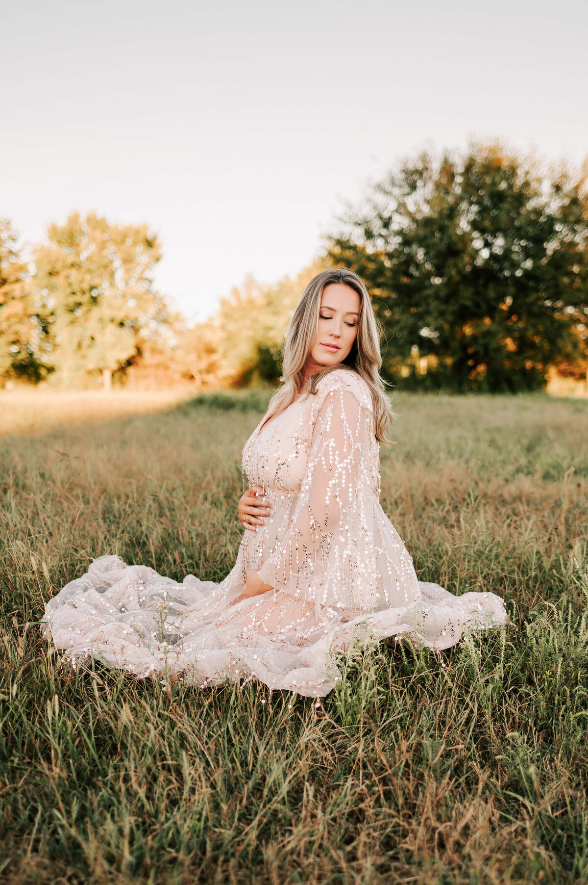 Springfield MO maternity photography of pregnant couple kneeling in field looking over her sholder holding her baby bump
