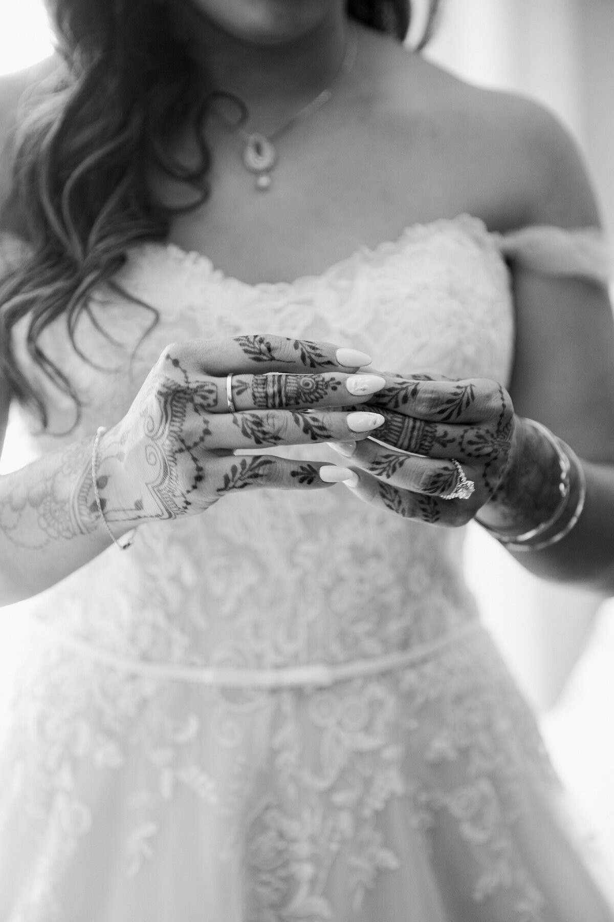 Portrait of a bride's hands on her wedding day in Dallas, Texas. Her hands are adorned with traditional patterns and artwork of her culture. Additionally, she is wearing an intricate, detailed, white dress, multiple bracelets, and a necklace.