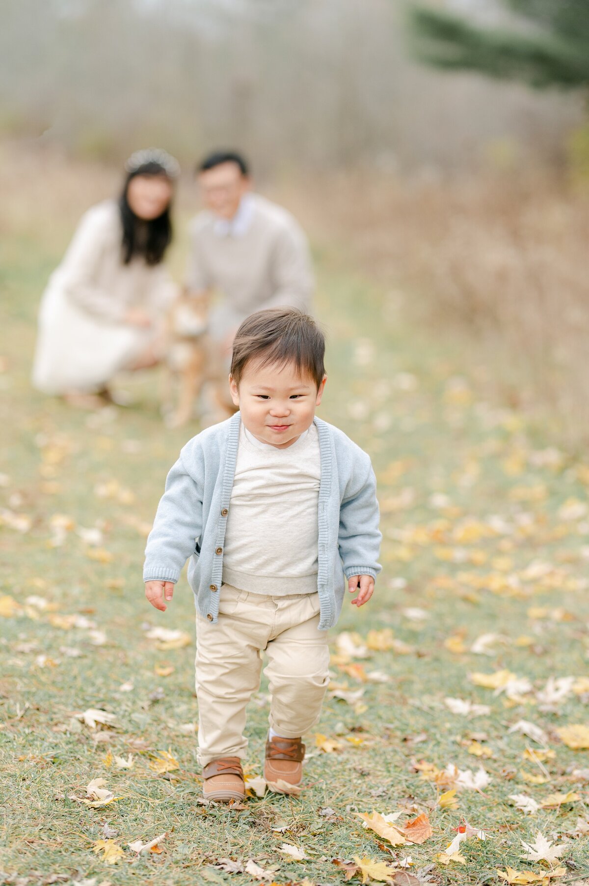 Little boy runs toward the camera while his parents are crouched down in the background