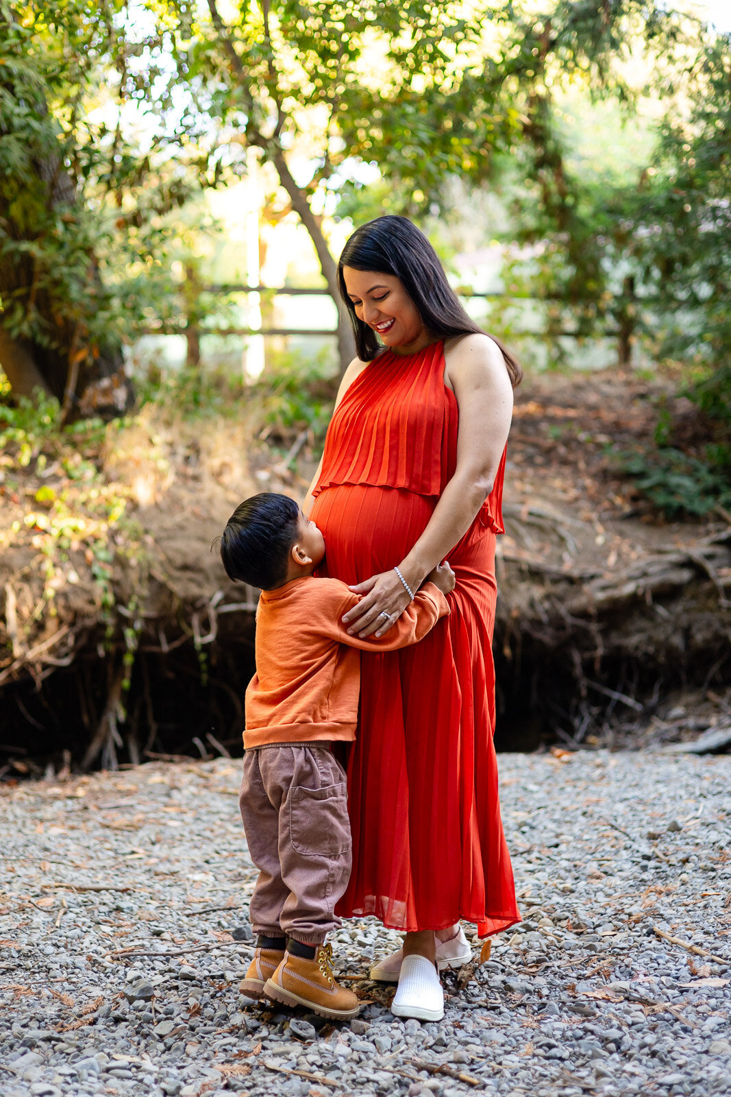 Pregnant woman standing in a creek bed, hugging her son who is embracing her belly – Ellobelle Photography