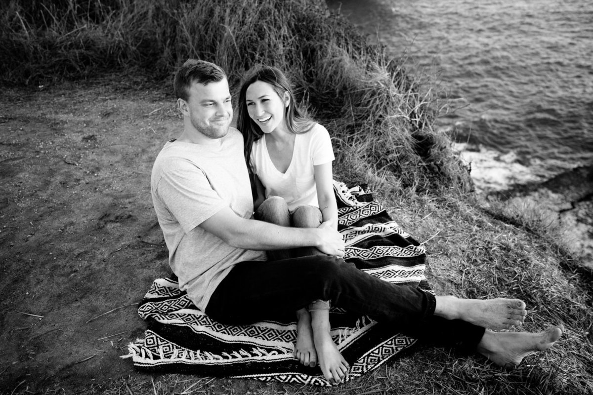 Deneffe studios image of engaged bride and groom on blanket, cliff overlooking beach