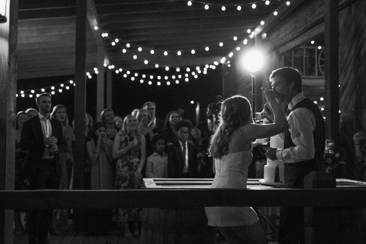 couple-feeds-each-other-cake-with-guests-in-background