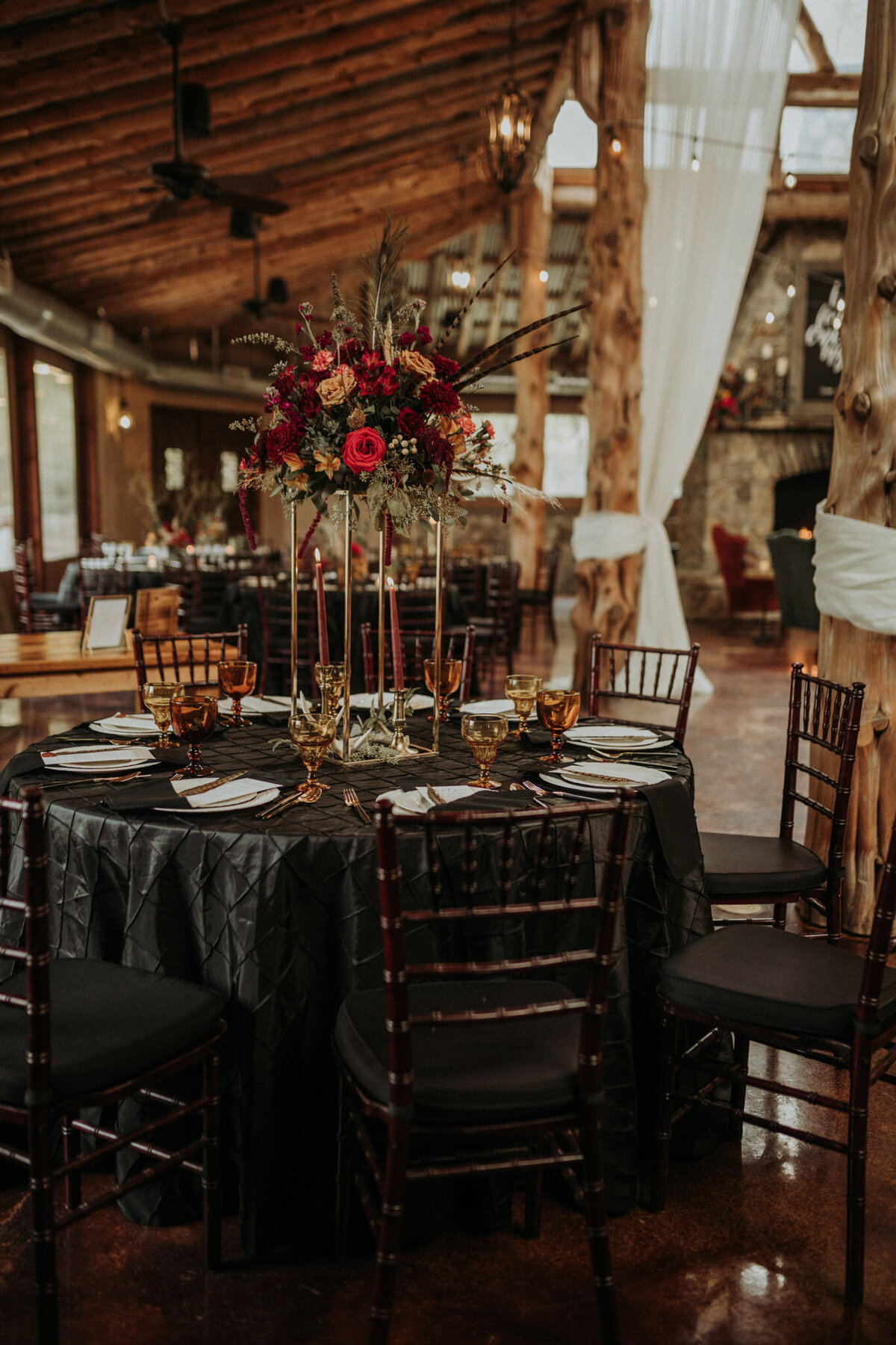 Wedding reception table decor with black linens red and tan flowers with bird feathers and cowhides