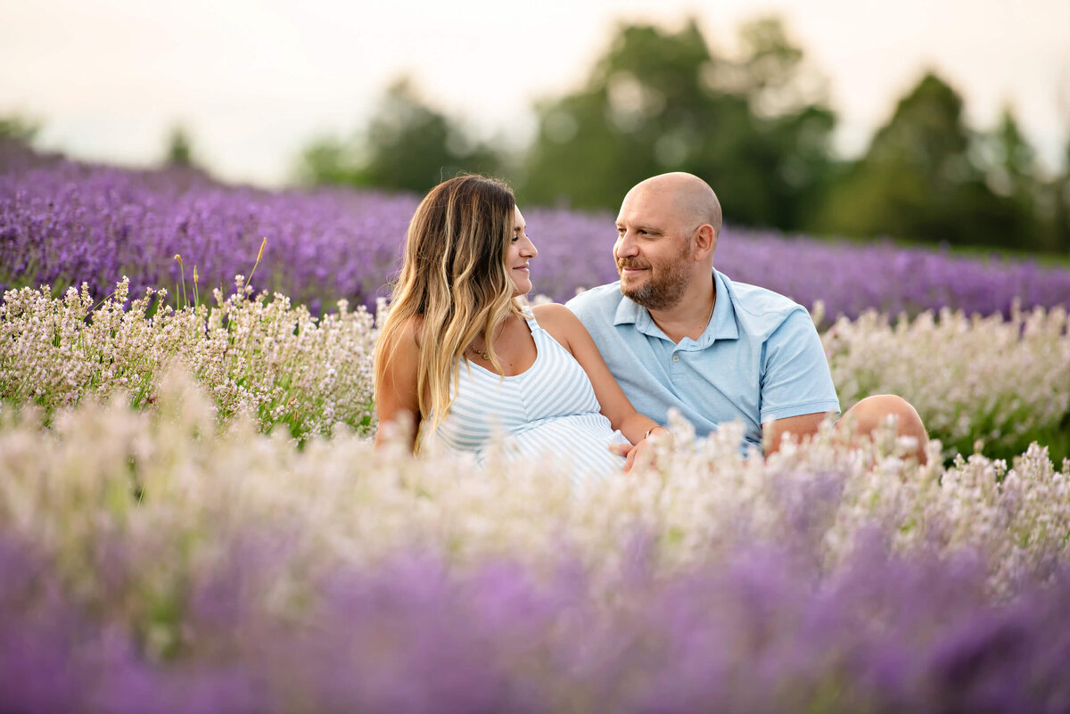 husband and wife looking at each other sitting in the lavender for their Toronto maternity photography session