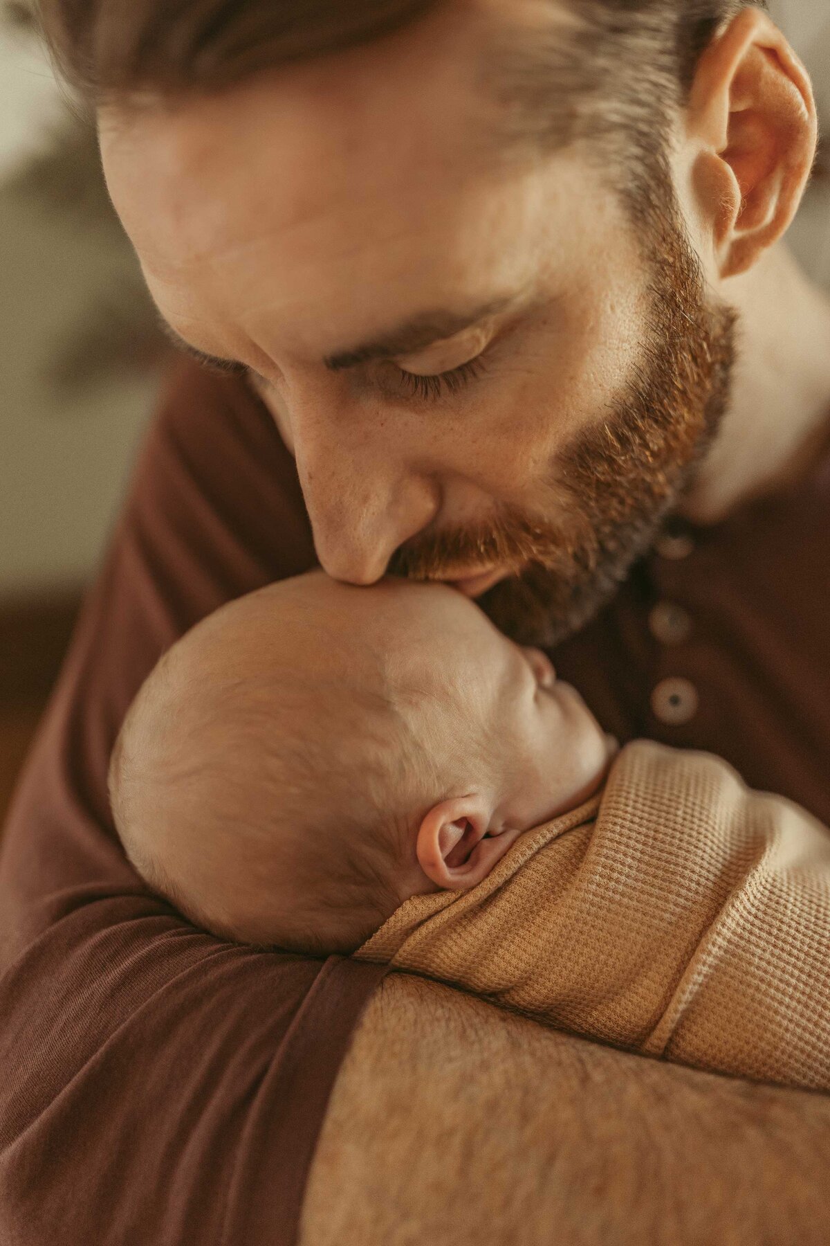 Man with beard kissing baby on he forehead softly.