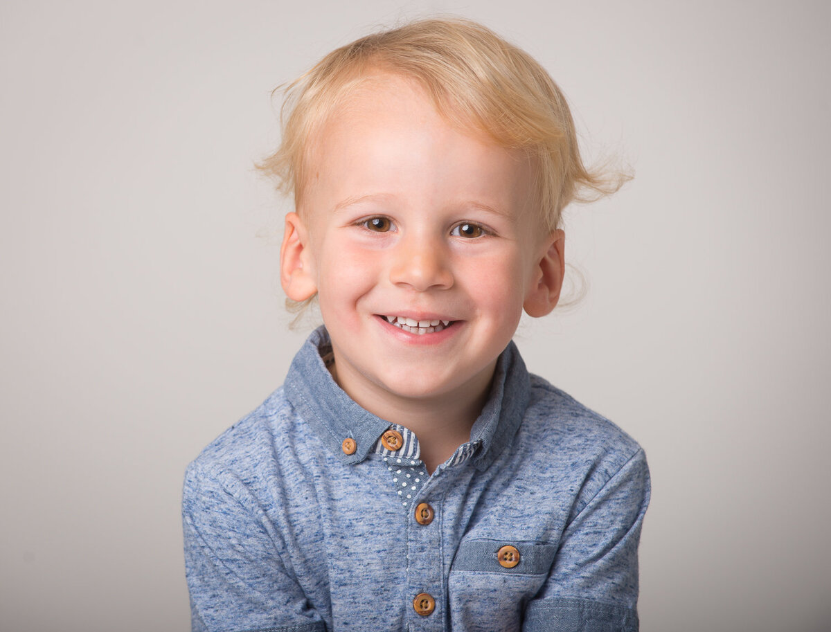 portrait of a toddler boy with blonde hair smiling wearing a blue t shirt