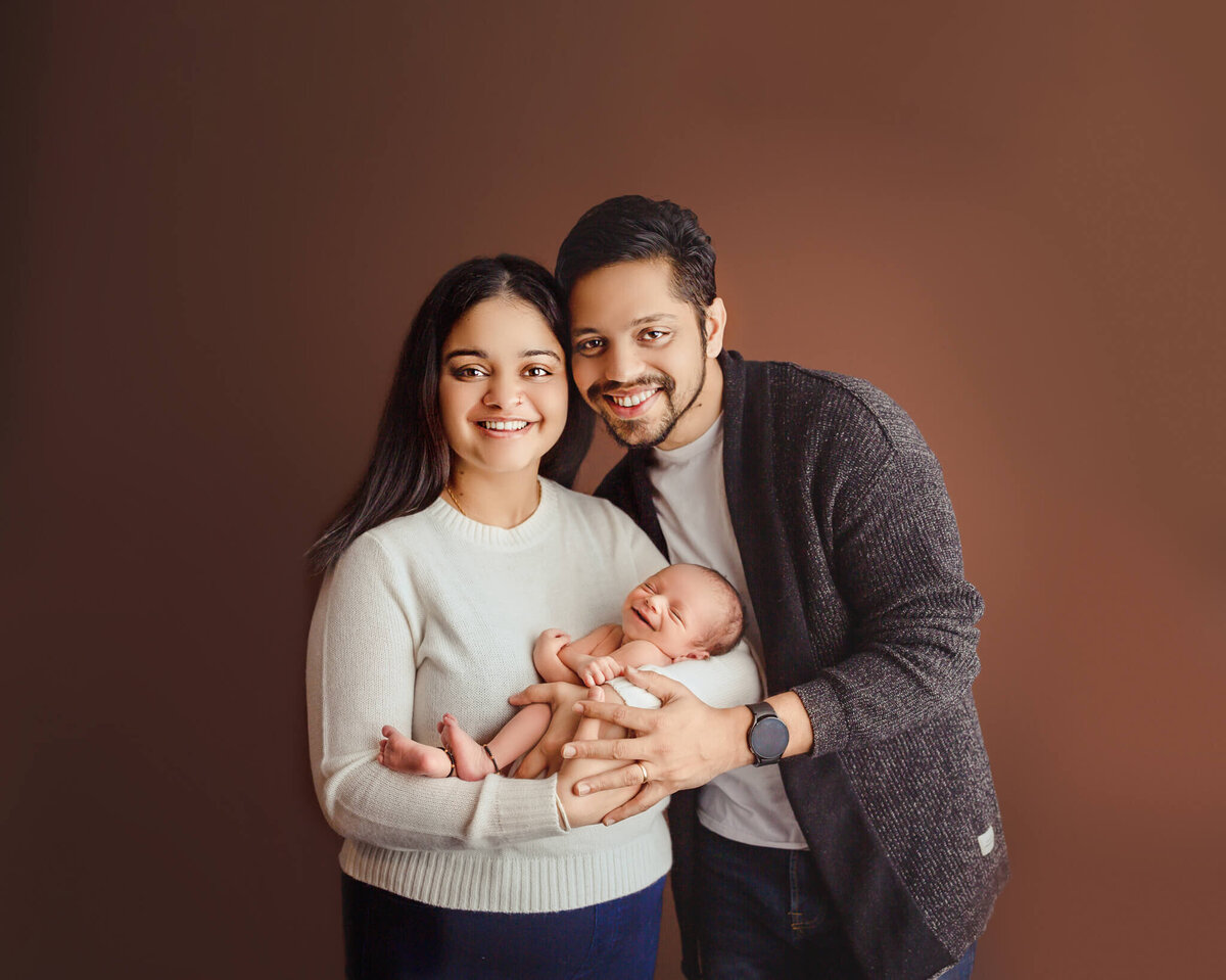 newborn baby has big smile while being held by new parents in niagara photography studio