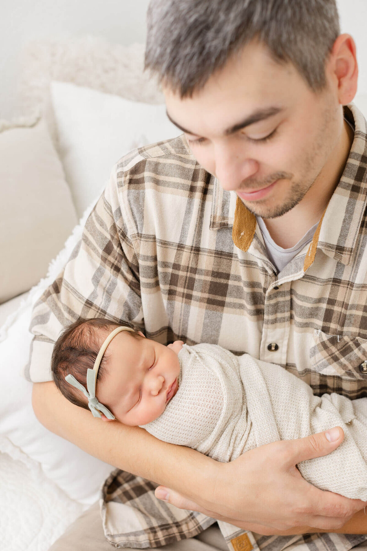 Dad holding newborn baby girl in his arms and looking down at her while she is fast asleep