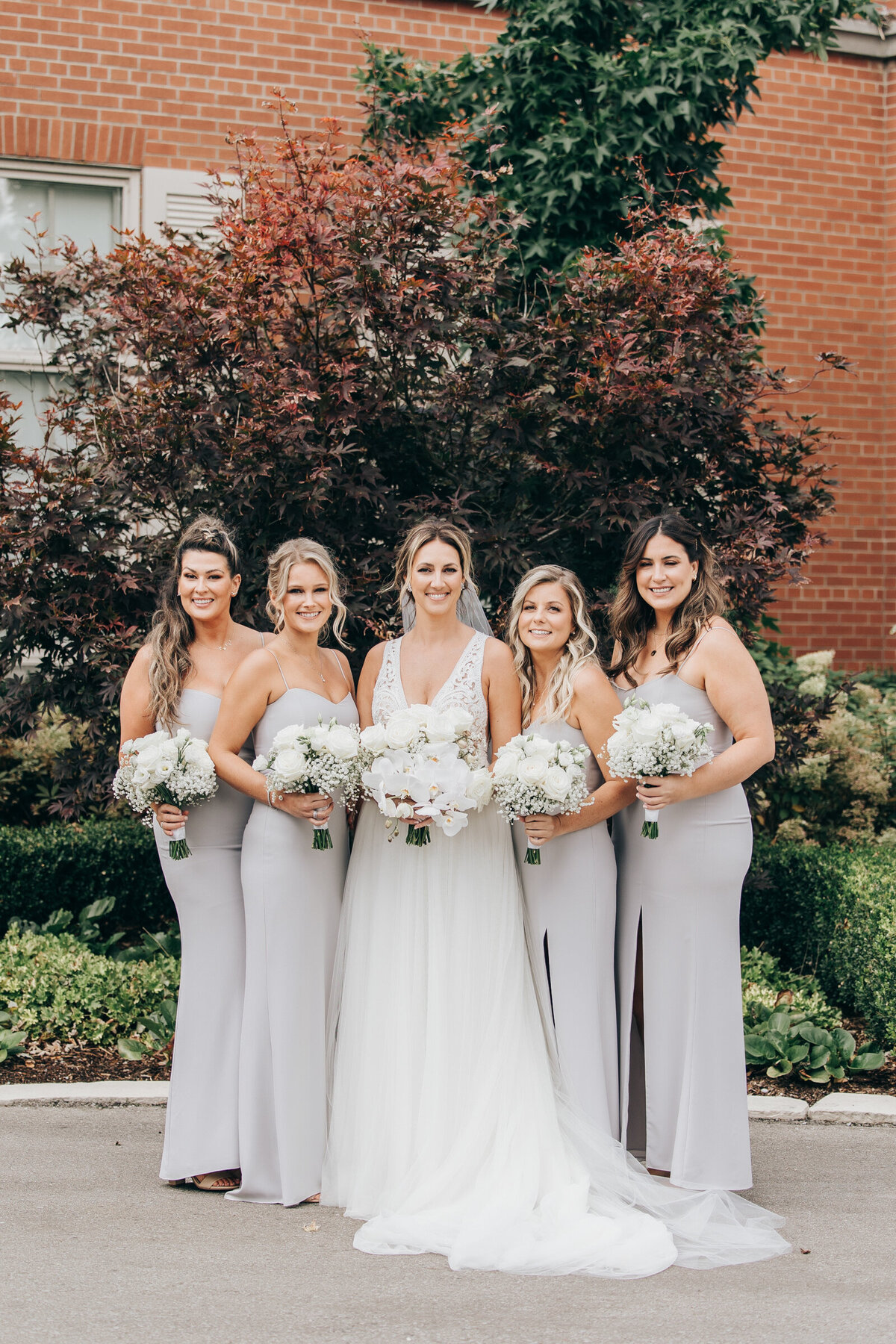 Bridesmaids holding white bouquets posing for traditional photos