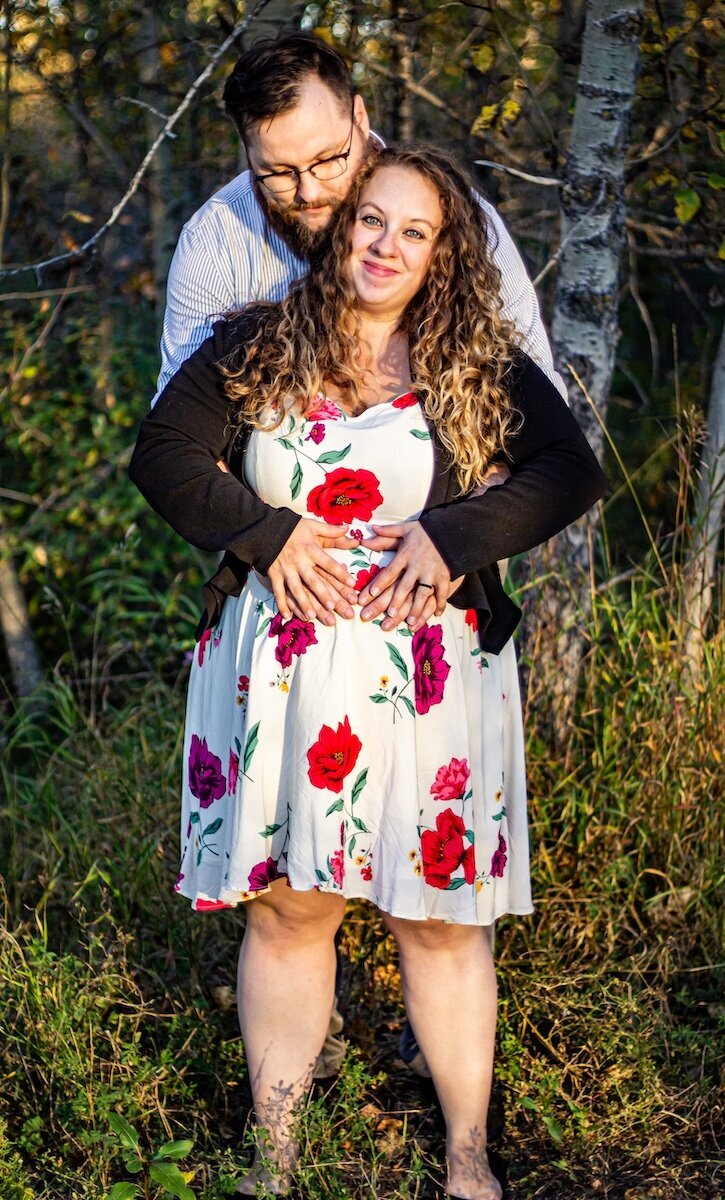 a husband hugs his pregnant wife from behind