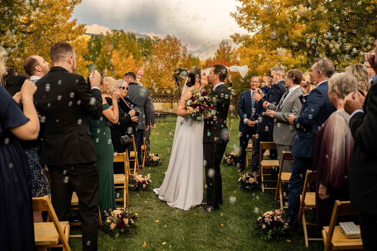 Bride and groom kiss surrounded by bubbles.