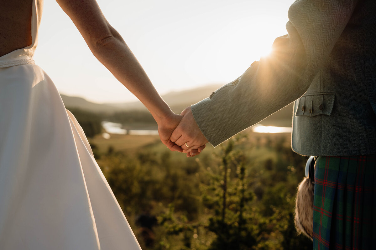 A couple are photographed holding hands during golden hour in the Scottish landscape.
