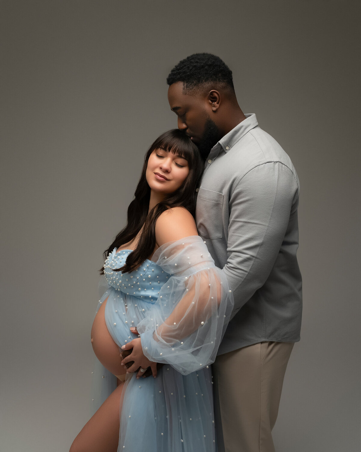 Soft and romantic studio portrait of an expecting couple with the mom-to-be in a blue pearl-detailed maternity gown.