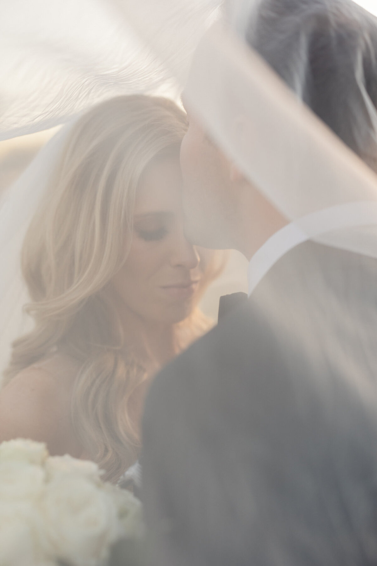 Bride and groom under wedding veil closing eyes