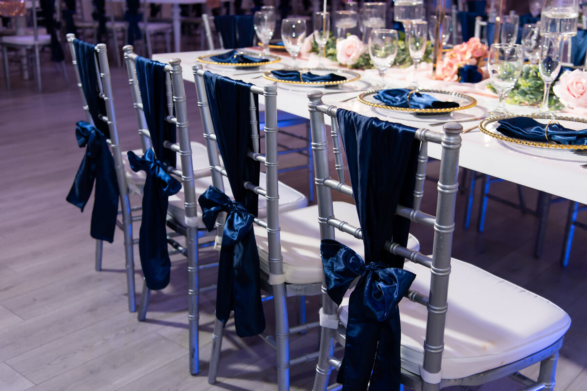 navy and blush design reception of silver chiavari chairs each with a navy satin sash tied horizontally in a bow