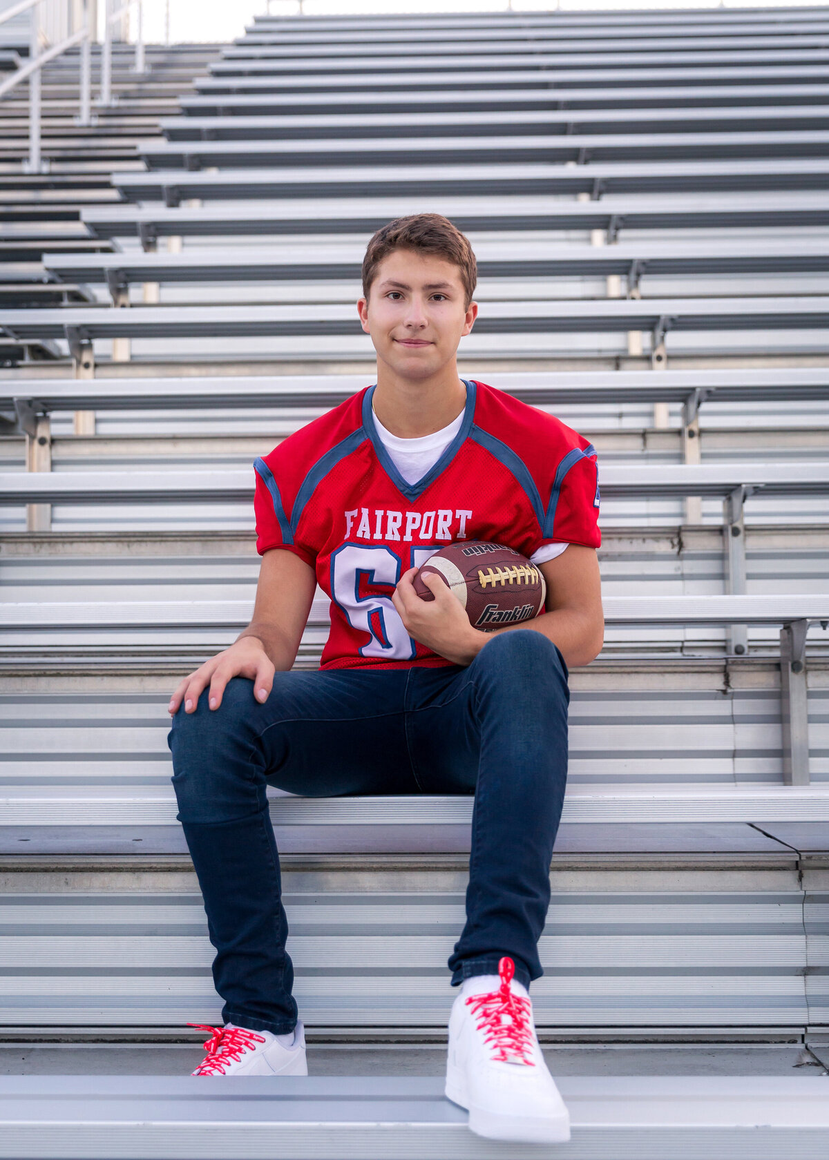 Fairport high school senior guy pictures on the bleachers with football