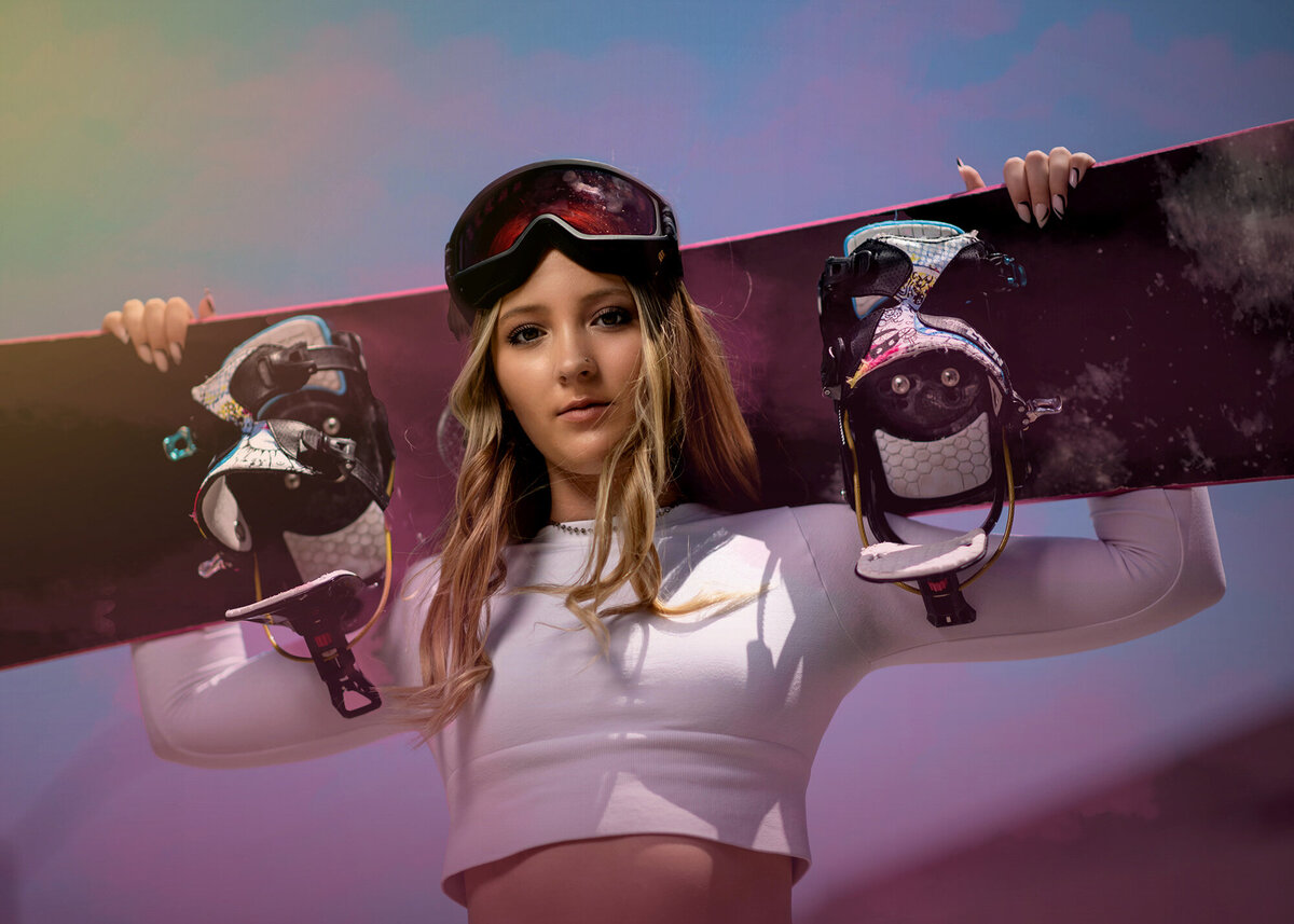 A high school senior in a white top holds a snowboard behind her head