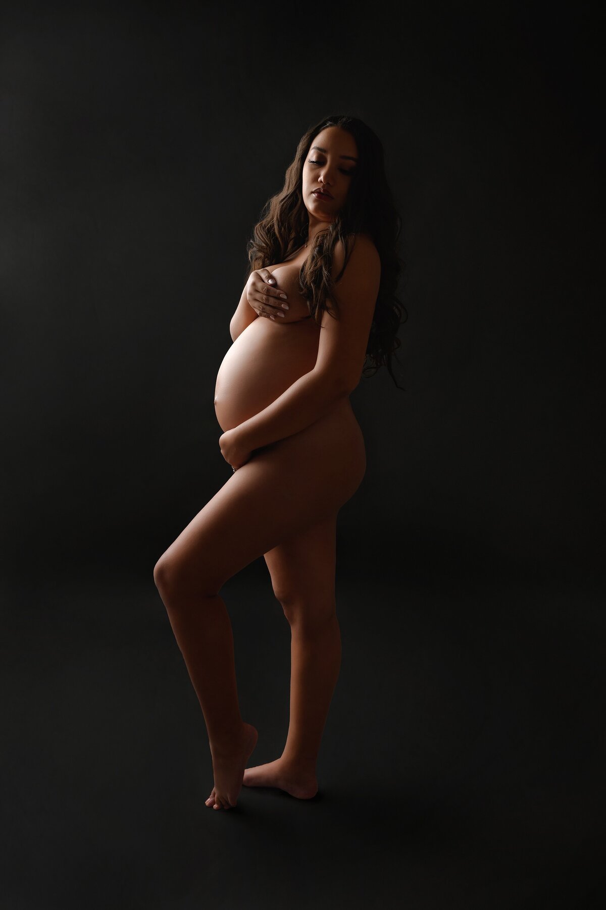 Pregnant model poses in moody lighting for intimate maternity photo.