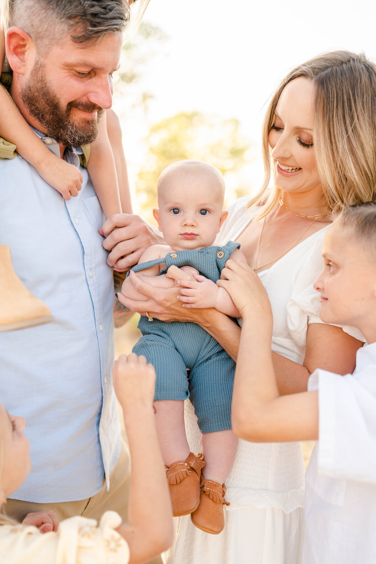 A young child dressed in cotton suspenders  is being held by his family in a pampas grass field photographed by Bay area photographer, Light Livin Photography.