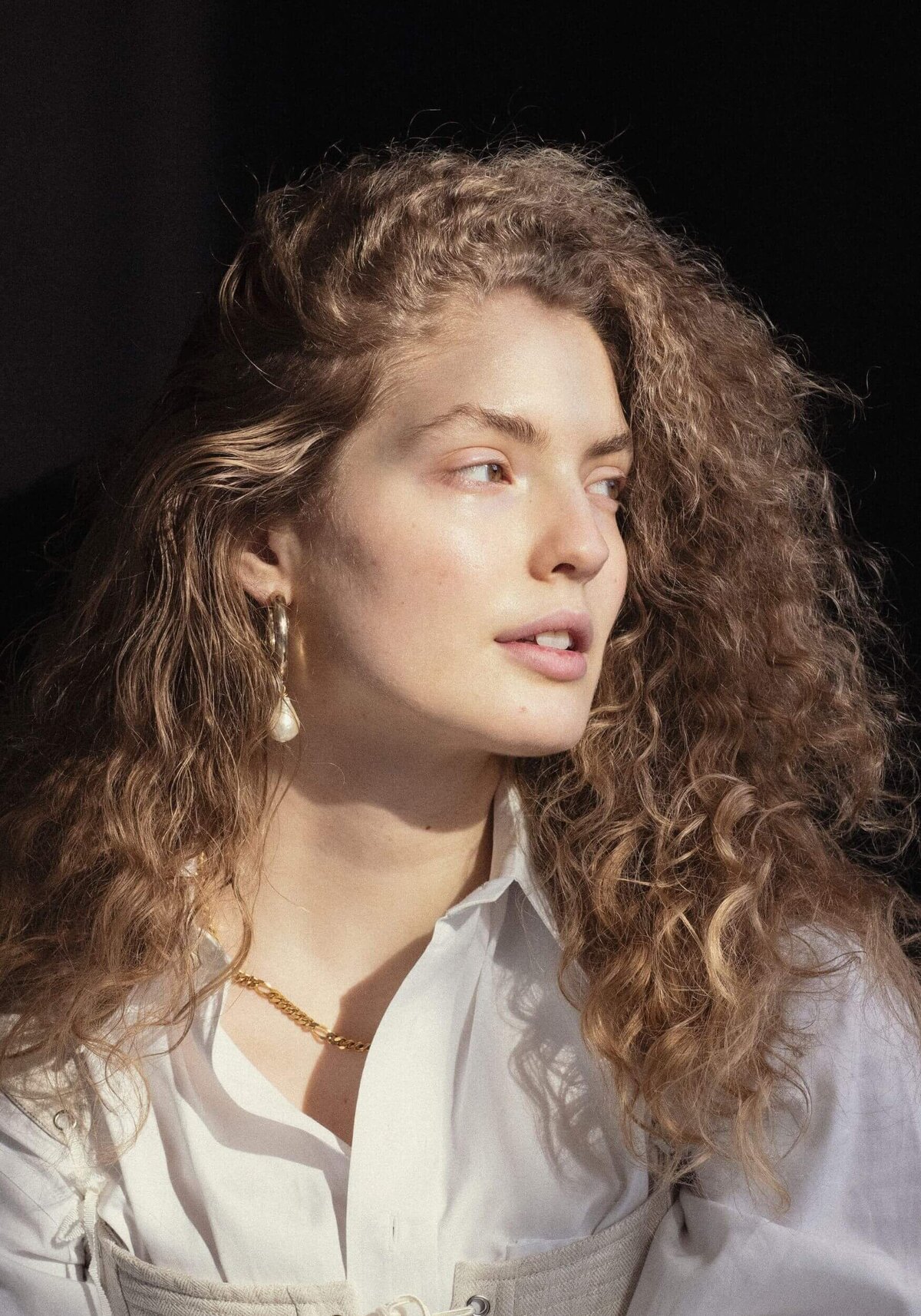 Fashionable young female model sitting in dark room and looking away
