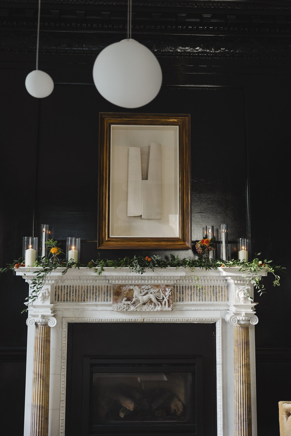 A white mantel around a fireplace decorated with florals and candles 