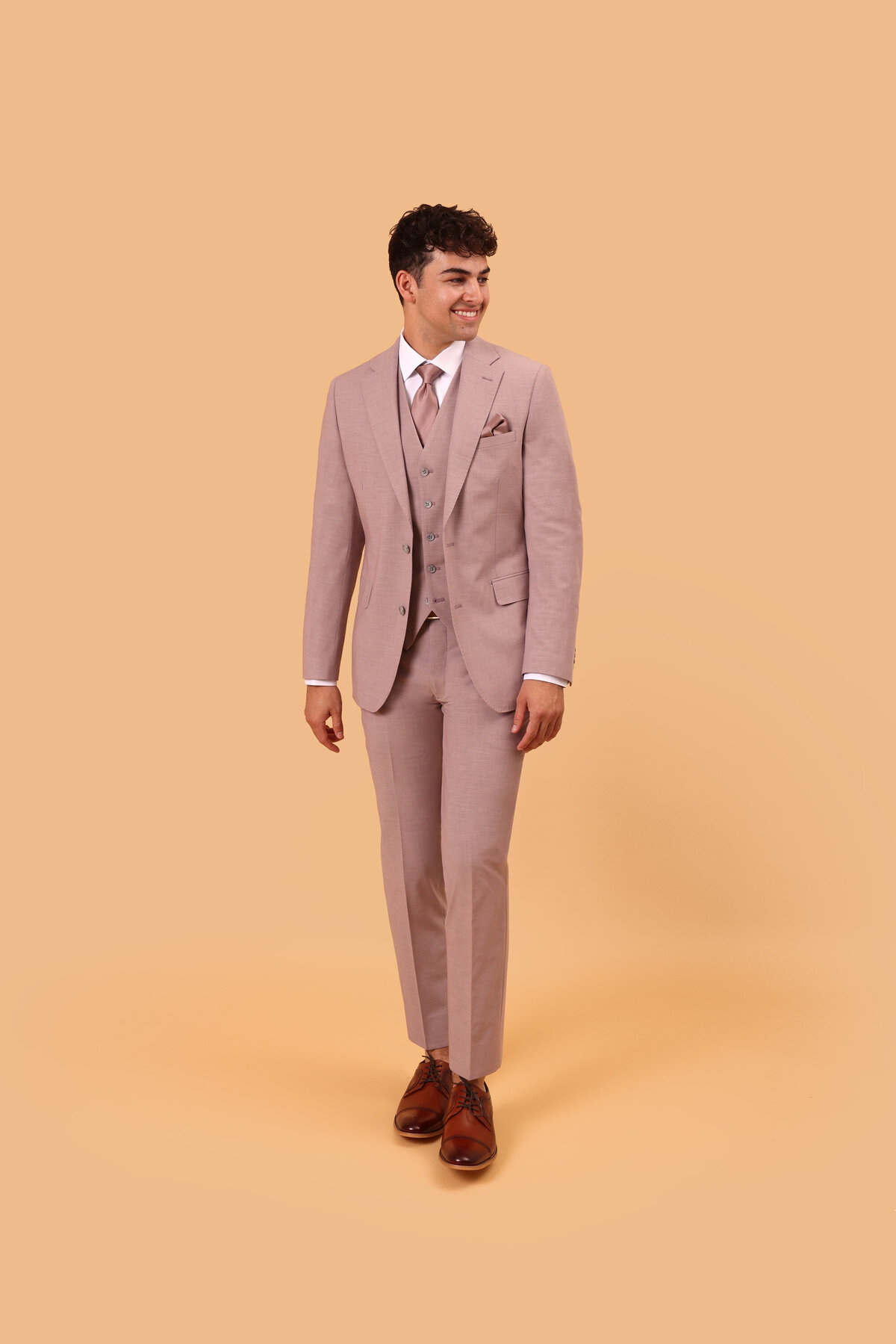 A young man posing in a linen blend suit against a burnt orange background for prom