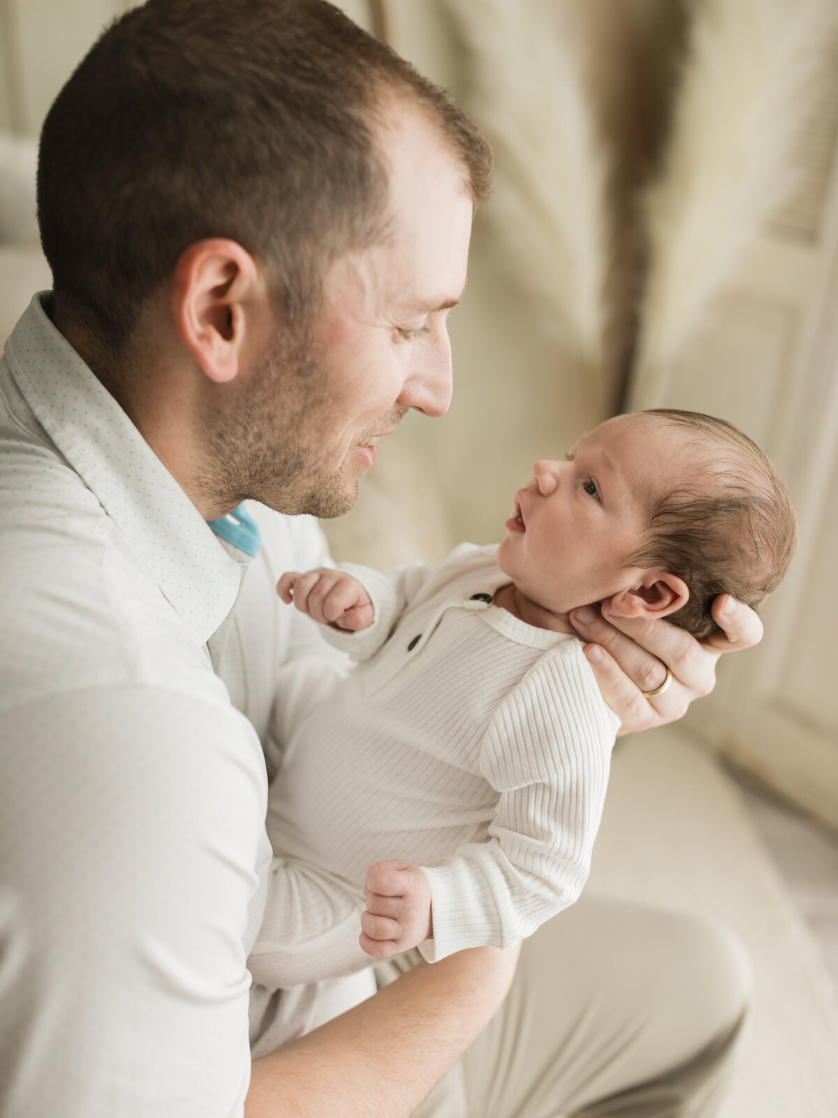 dad holding newborn baby boy in white onesie for studio photoshoot 