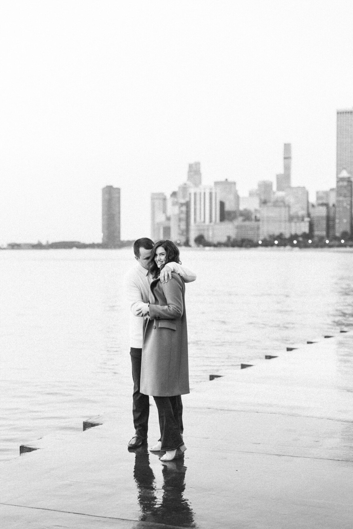 engaged couple standing in front of Chicago skyline in a black and white photo taken by destination and Chicago, Illinois wedding photographer Alex Ferreri