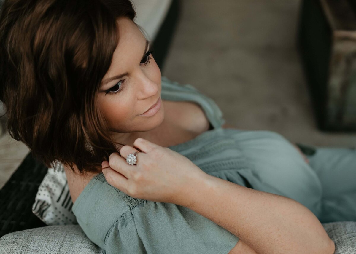 A pregnant woman sitting on a couch, displaying her engagement ring. Captured by a Pittsburgh maternity photographer.