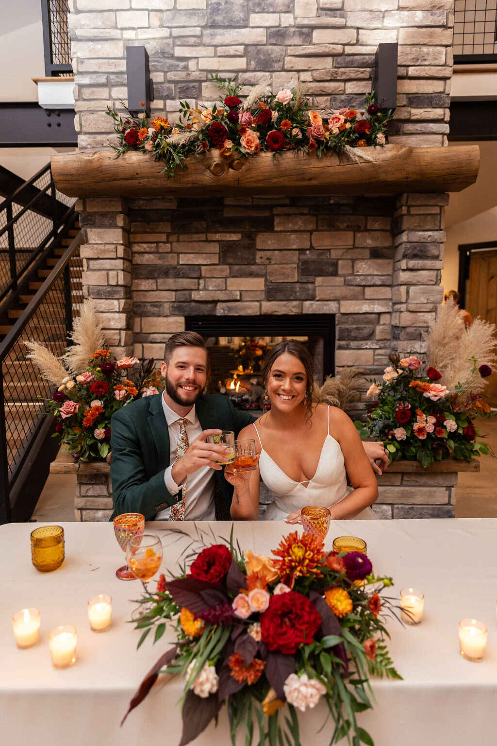 Bride and groom at their sweetheart table surrounded by burgundy, blush, orange, and peach flowers on their wedding day at Bonnie Blues Event Venue.