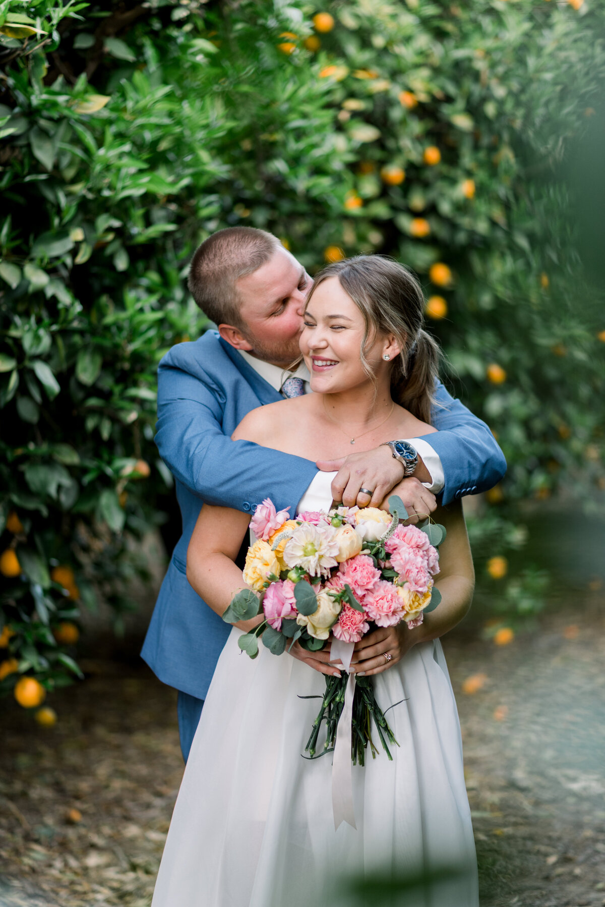 bride and groom kissing in between the orange groves in lorimar winery