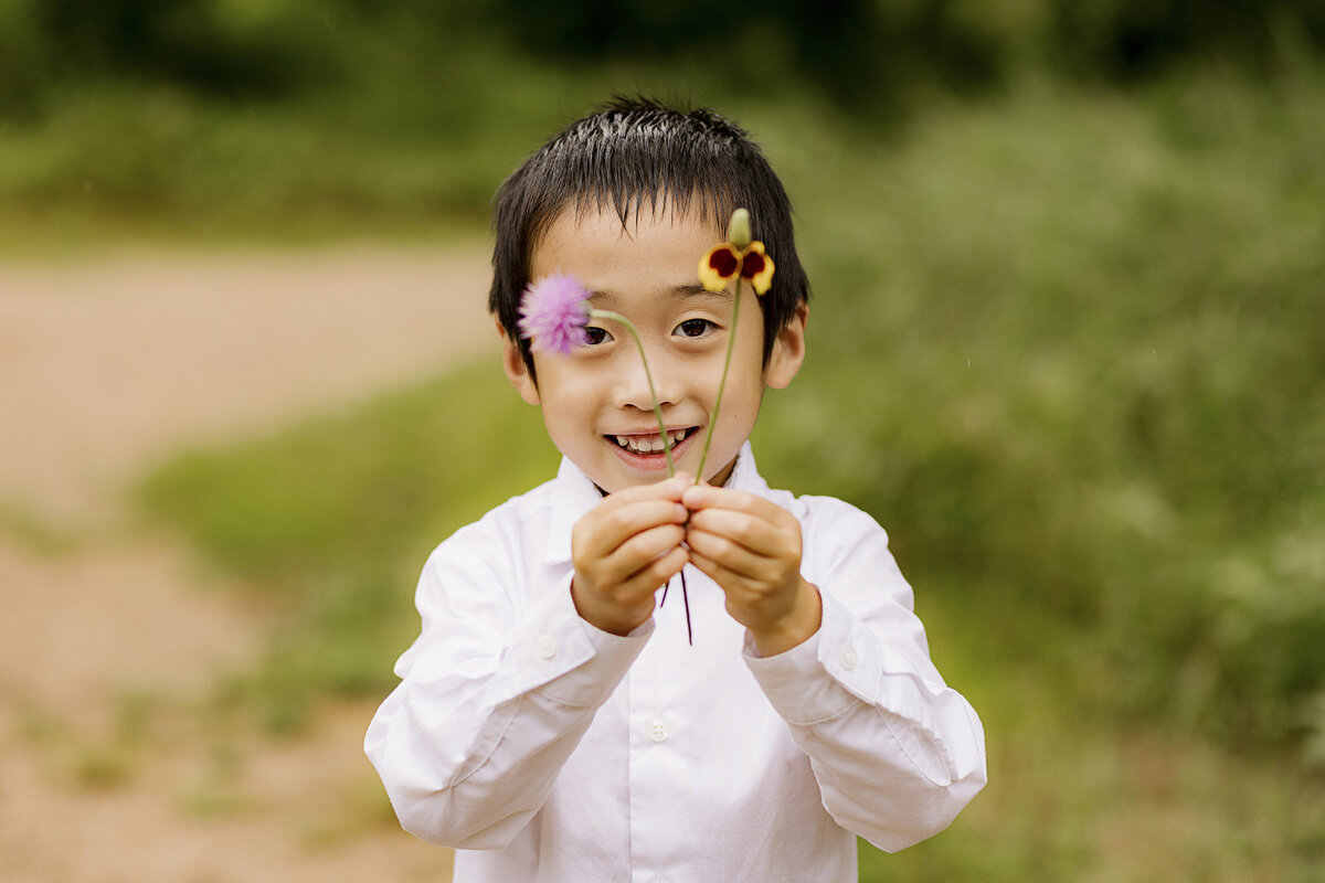young boy holding wild flowers and smiling