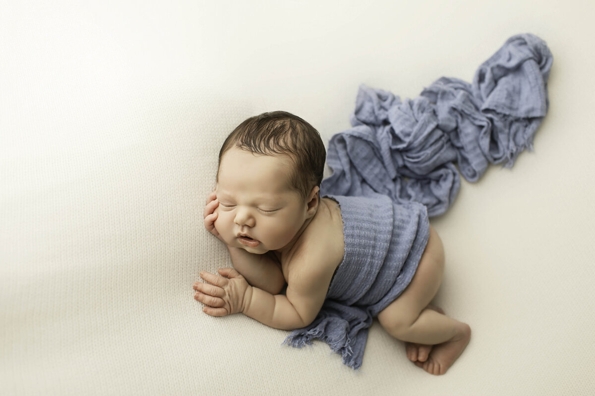 Newborn baby boy peacefully wrapped in a soft blue fabric, resting comfortably with a serene expression, creating a classic and timeless portrait