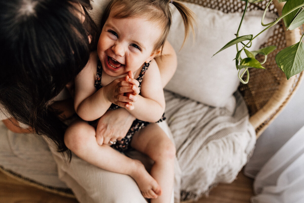 Mother holds laughing daughter on chair at studio photography