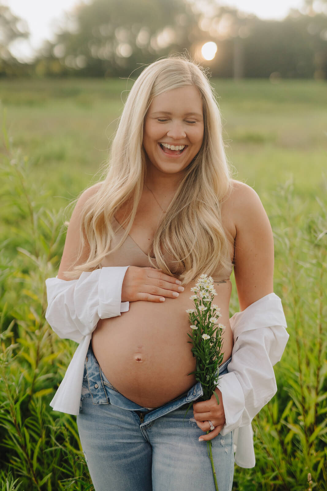Woman showing bare baby bump and holding bouquet of flowers at  maternity session in Finger Lakes, New York