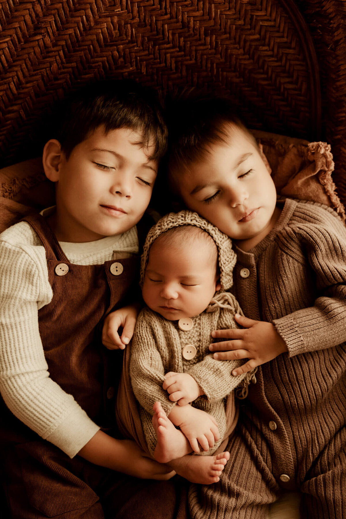 Two brothers snuggle their newborn baby brother as he sleeps.
