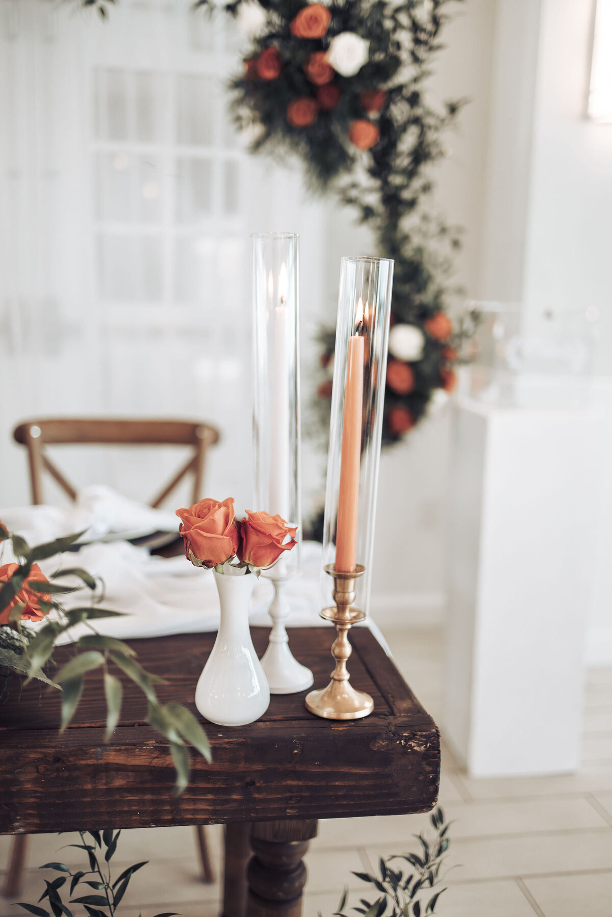 orange roses in a white vase and a candle on a wooden table