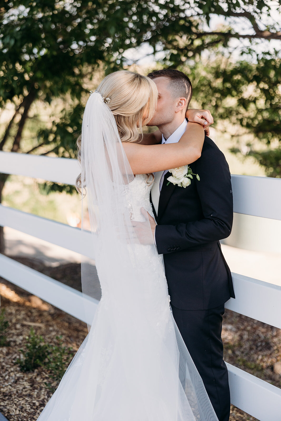 Couple embrace along a white fence line during their wedding photos at Brindabella Hills Winery