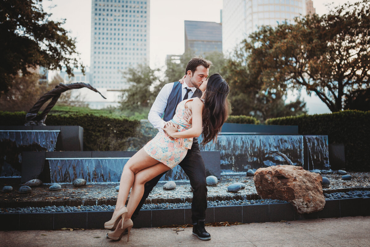 Couple sharing a dip kiss in front of a fountain and city skyline during an Orlando engagement photo session.