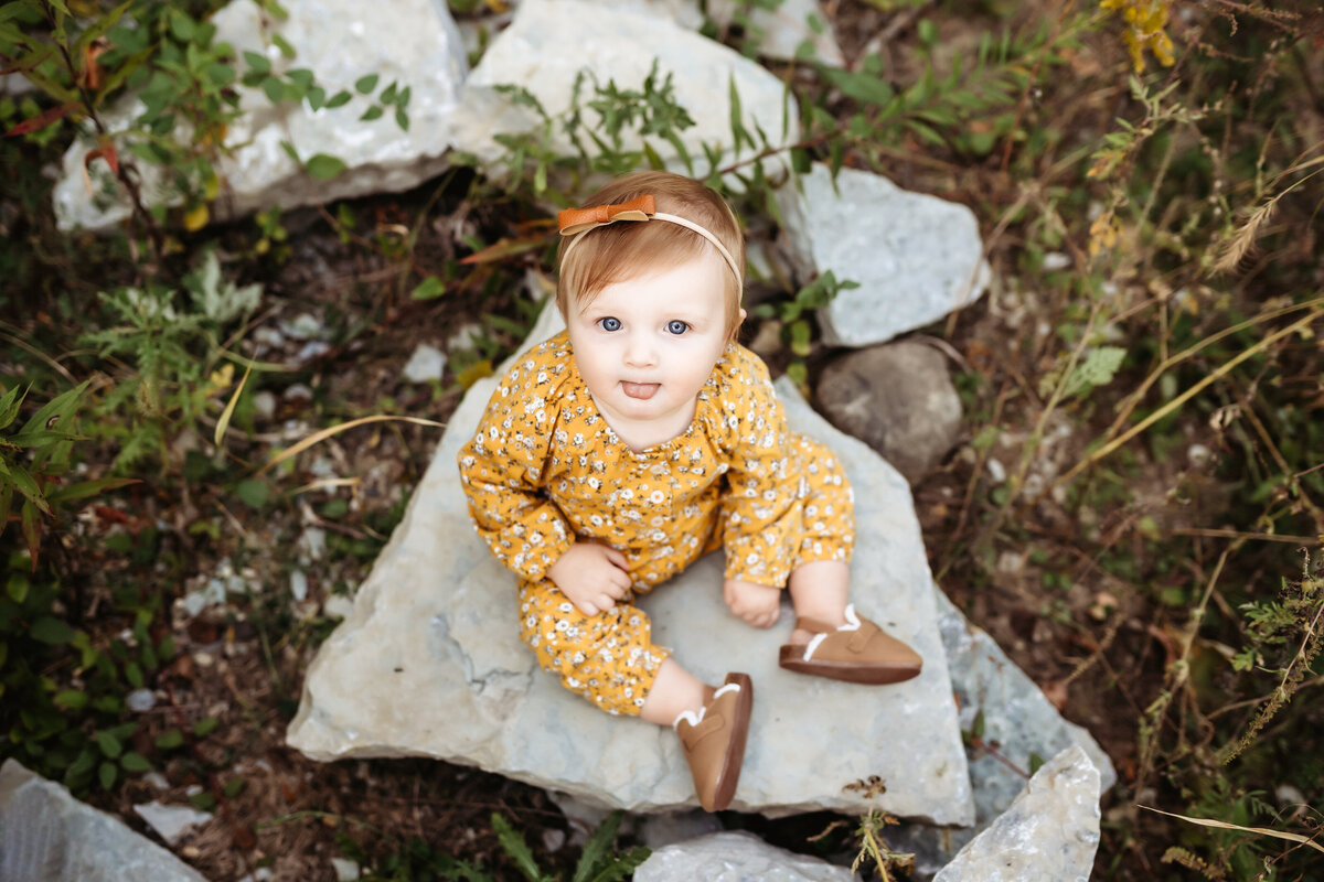 Little girl in yellow outfit sitting on a rock