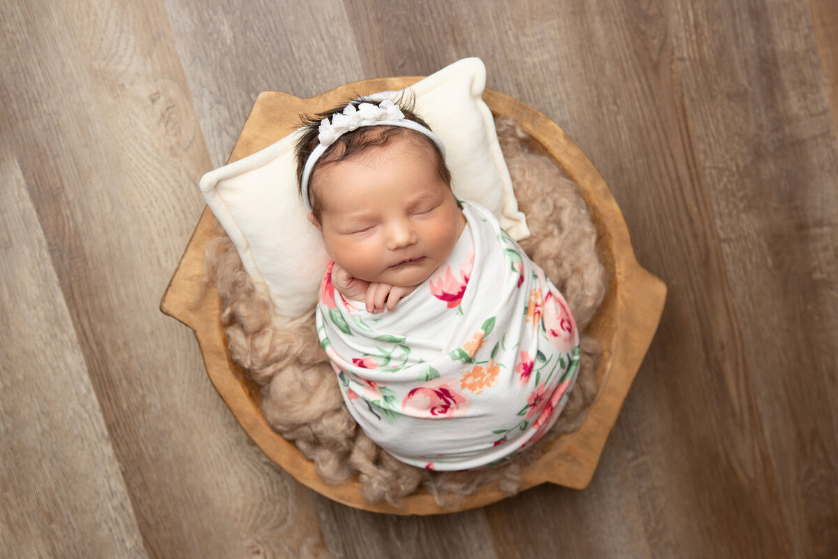 Floral wrapped newborn girl in a wooden bowl