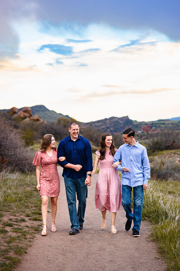 A family walks with arms linked with mountains in the background.